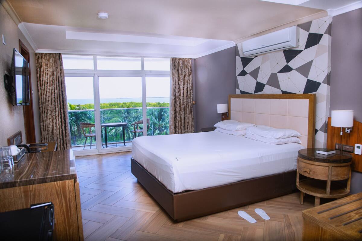 Habitación de hotel con una cama grande, un escritorio de madera, un televisor y un balcón con vistas.