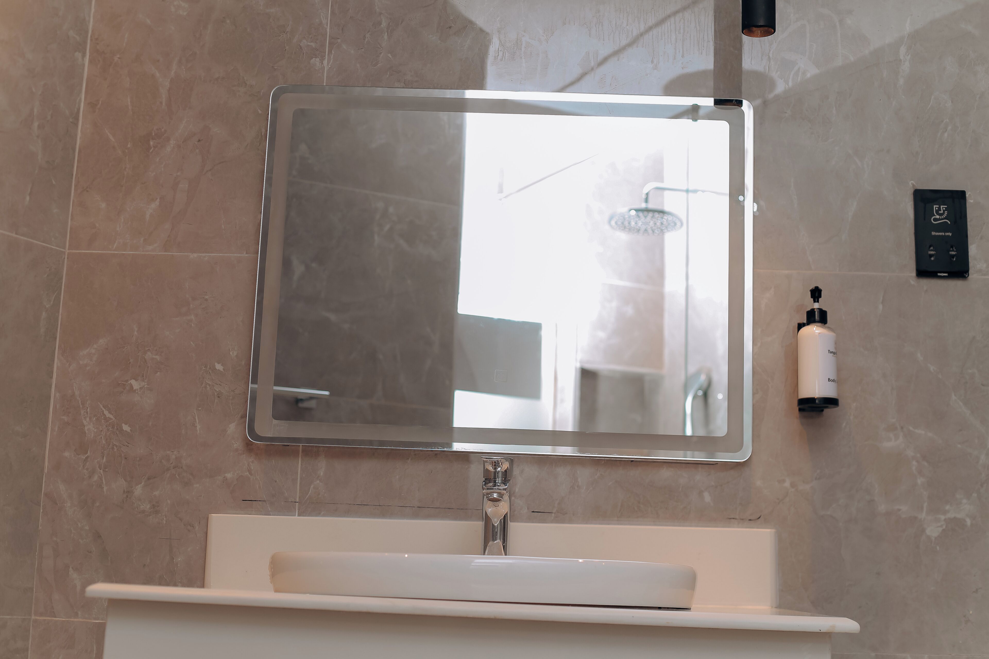 A bathroom with a large mirror, a sink, and a wall-mounted soap dispenser.