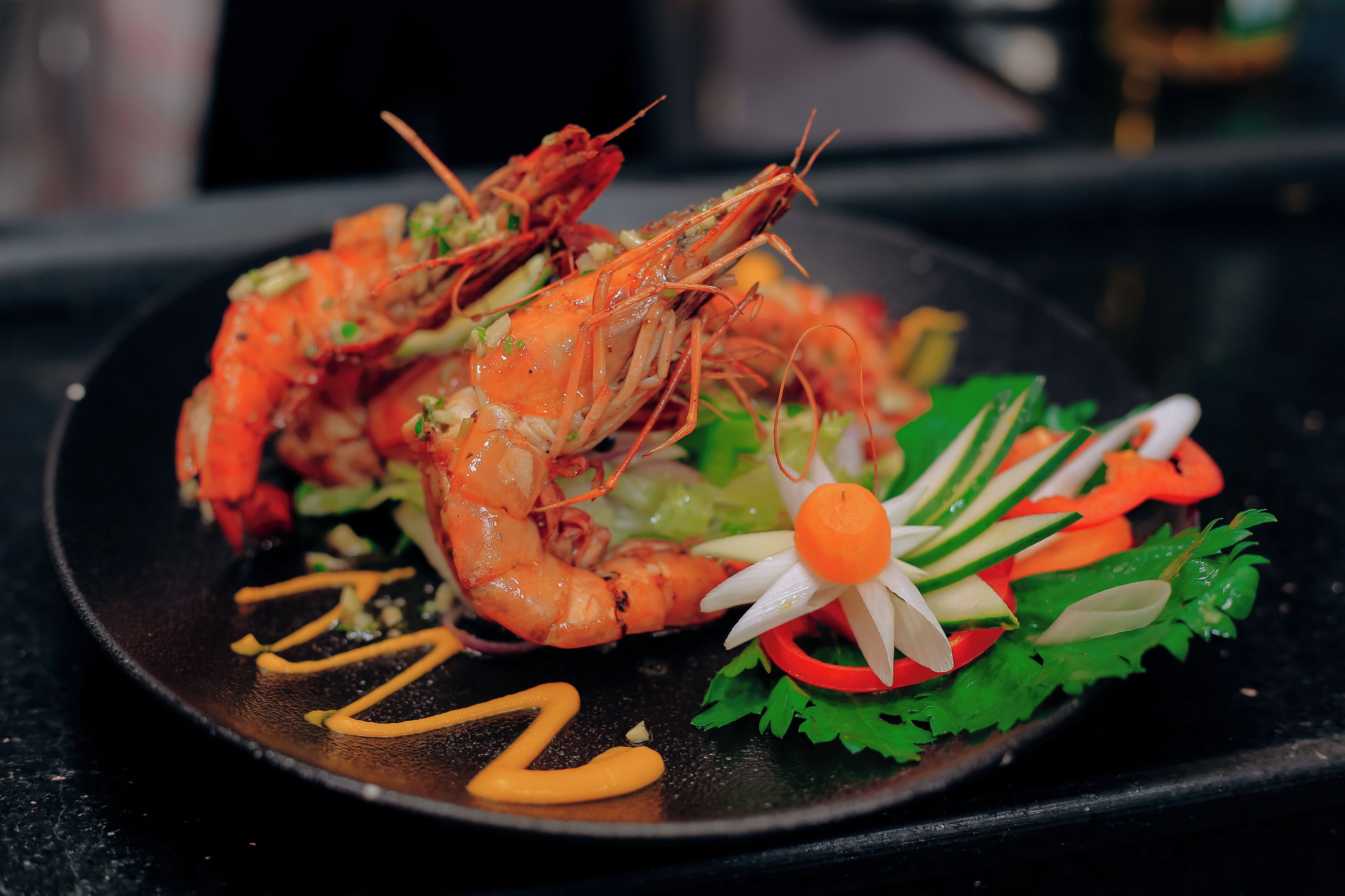A plate of cooked shrimp with vegetables and a decorative flower on a black plate.