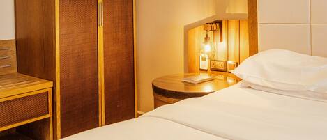 Habitación de hotel con cama, armario de madera, mesita de noche con lámpara y pared con estampado geométrico.