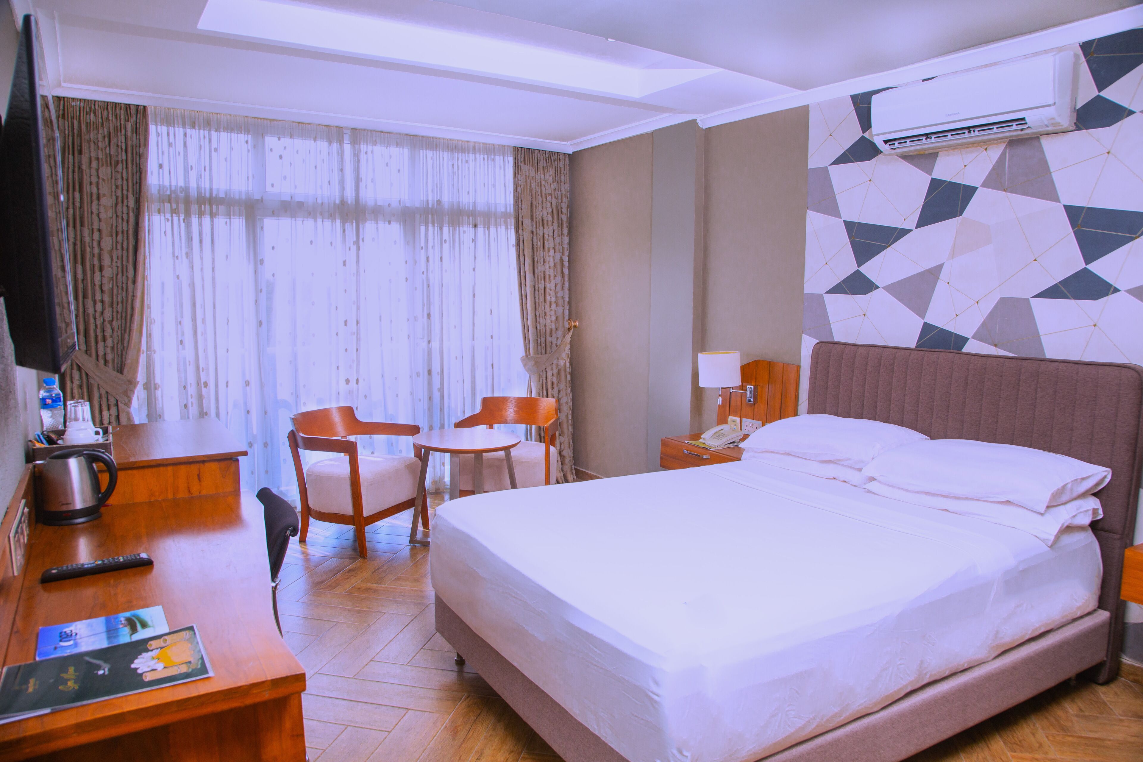 A hotel room with a bed, a desk, a chair, a small table, and a television.