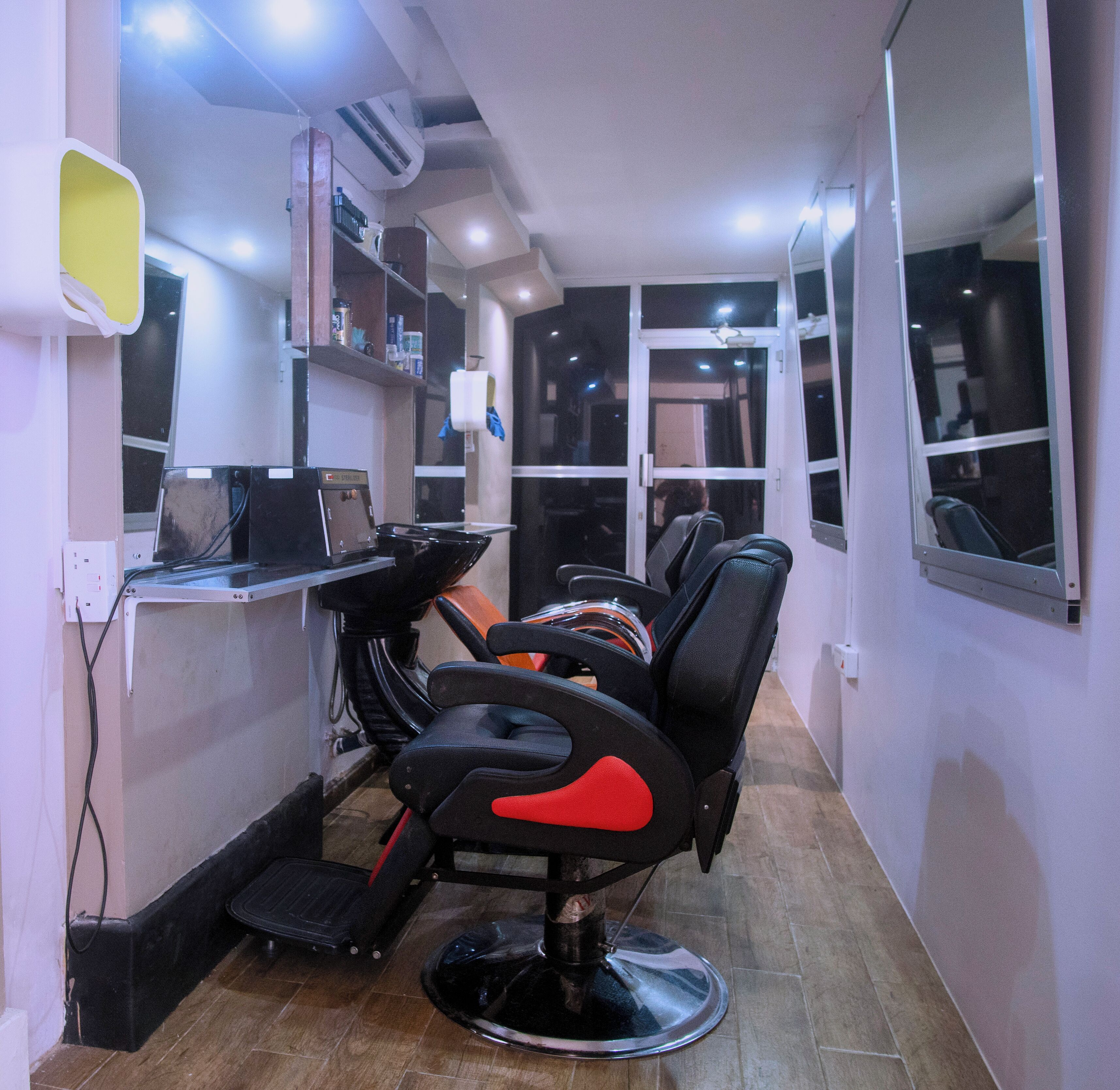 A narrow hallway with a salon chair, a mirror, and shelves with various items.