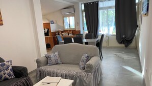 A living room with a grey sofa, a white table, and a kitchen in the background.