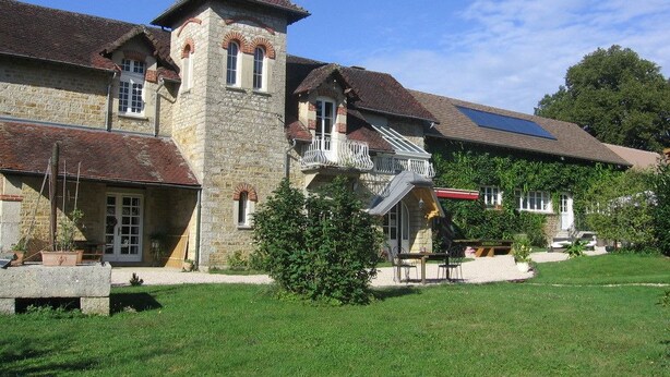 A stone building with a tower, a balcony, and a covered patio area.
