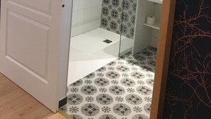 A modern bathroom with a glass shower enclosure, patterned tiles, and a white door.
