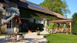A stone house with a covered patio, a gravel driveway, and a wooden pergola.