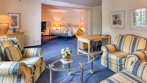 A room with a bed, two sofas, a glass coffee table, and a small table with a lamp. - Hotel Restaurant Alt Vellern (Beckum)