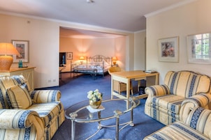 Una habitación con una cama, dos sofás, una mesa de centro de vidrio y una mesita con una lámpara.