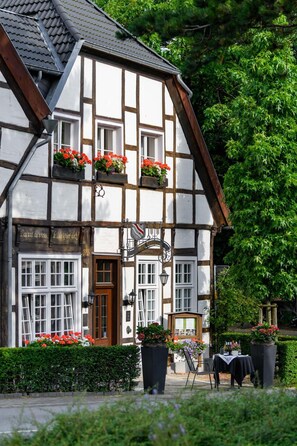 A traditional half-timbered building with flower boxes on the windows, a signboard, and a small outdoor seating area. - Hotel Restaurant Alt Vellern (Beckum)