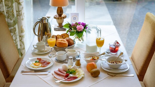 A breakfast table set with various dishes, including eggs, bacon, and pastries, along with drinks and condiments. - Hotel Restaurant Alt Vellern (Beckum)