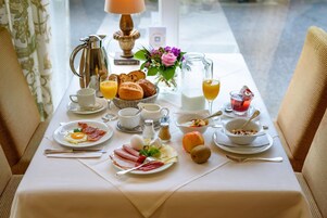 Una mesa de desayuno servida con diversos platos, como huevos, tocino y bollería, junto con bebidas y salsas.