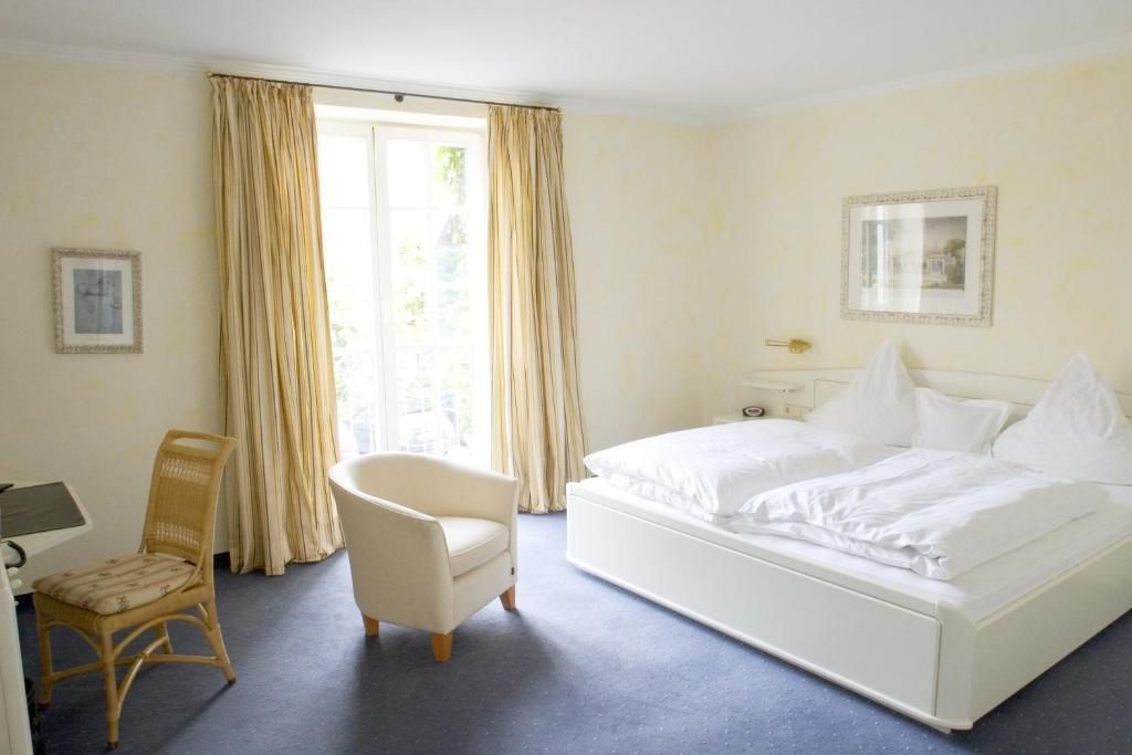 A hotel room with a bed, a chair, a desk, and curtains.