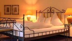 A neatly made bed with white linens and pillows, two bedside lamps, and two framed pictures on the wall. - Hotel Restaurant Alt Vellern (Beckum)