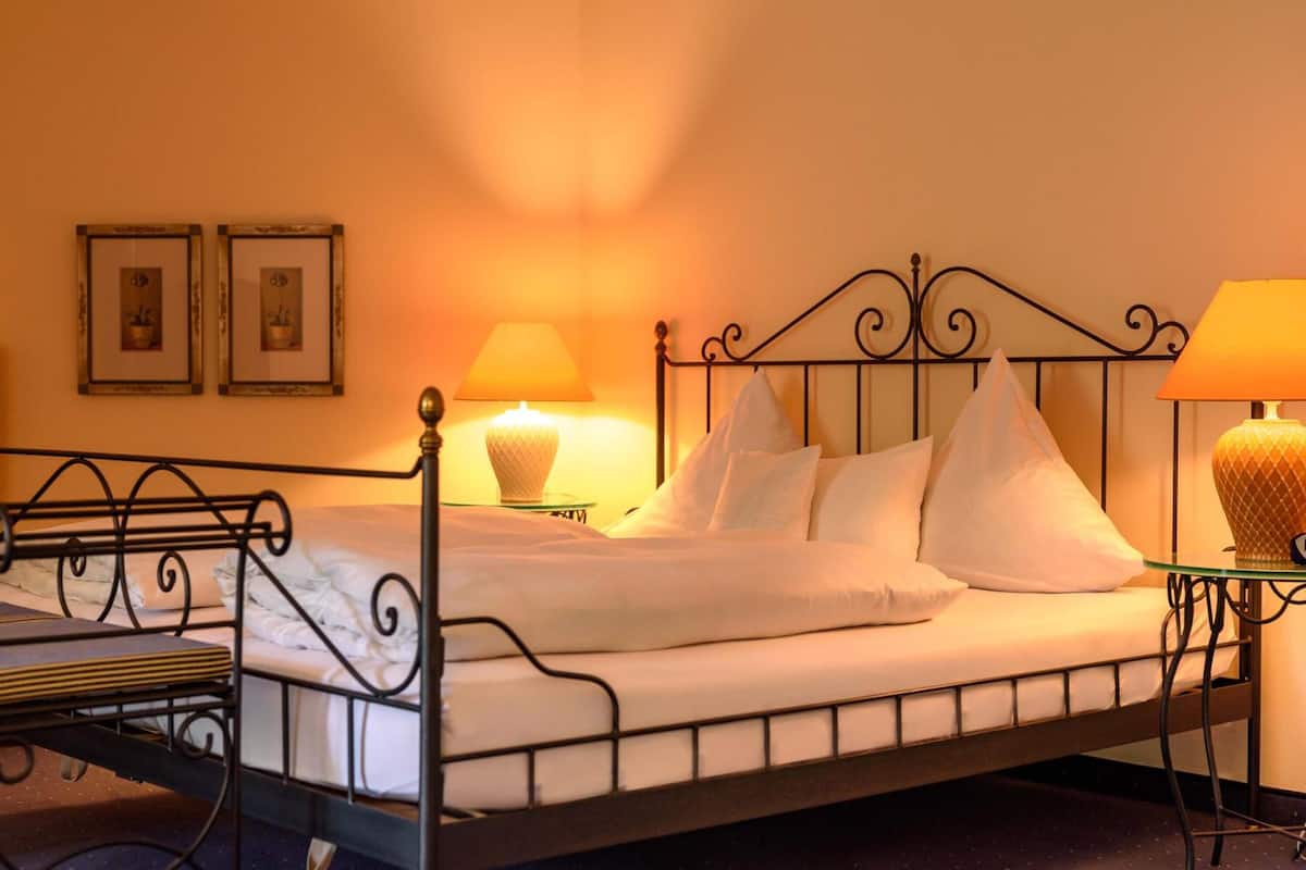 Un lit bien fait, avec du linge de lit blanc et des oreillers, deux lampes de chevet et deux tableaux encadrés au mur.