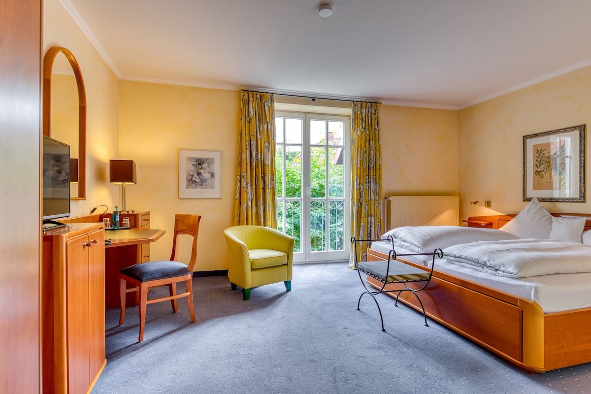 Une chambre d’hôtel avec un lit, un bureau, une chaise, une fenêtre avec des rideaux et un tableau encadré au mur.