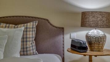 Una cama bien hecha con cabecera, una lámpara de noche y un jarrón decorativo sobre una mesita.