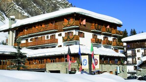 Un edificio de varios pisos con balcones de madera y techos cubiertos de nieve, frente a un paisaje montañoso.