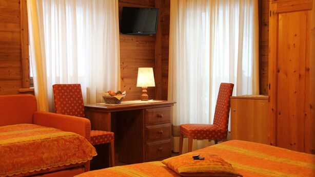 Una habitación acogedora con dos camas individuales, un escritorio con lámpara, televisión en la pared y una silla.