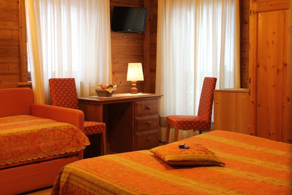 A cozy room with two single beds, a desk with a lamp, a television on the wall, and a chair.
