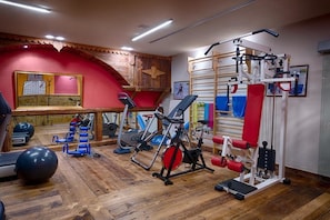 Un gimnasio con equipamiento de ejercicio, piso de madera y pared roja.