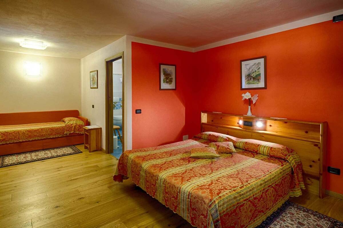 A room with a large bed, a smaller bed, and a bench. There are two framed pictures on the walls.