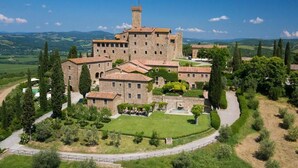 Un castello storico con diversi edifici, circondato da vegetazione lussureggiante e un sentiero sinuoso.