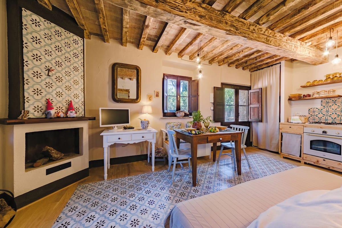 A cozy room with a fireplace, a dining table with chairs, a kitchen area with an oven, and a large window.