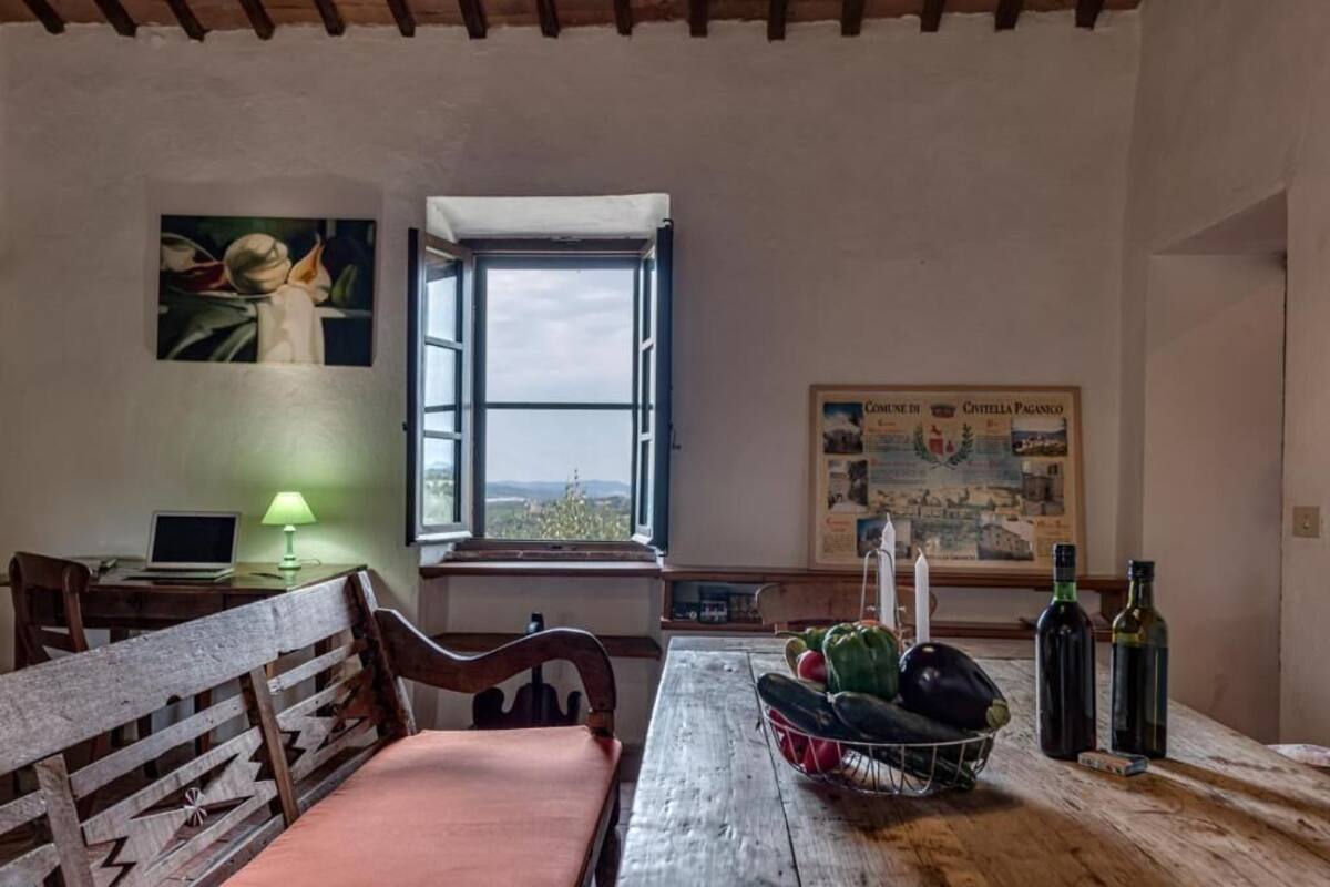 A rustic room with a wooden table, a laptop, a lamp, a window with a view, and a framed map on the wall.