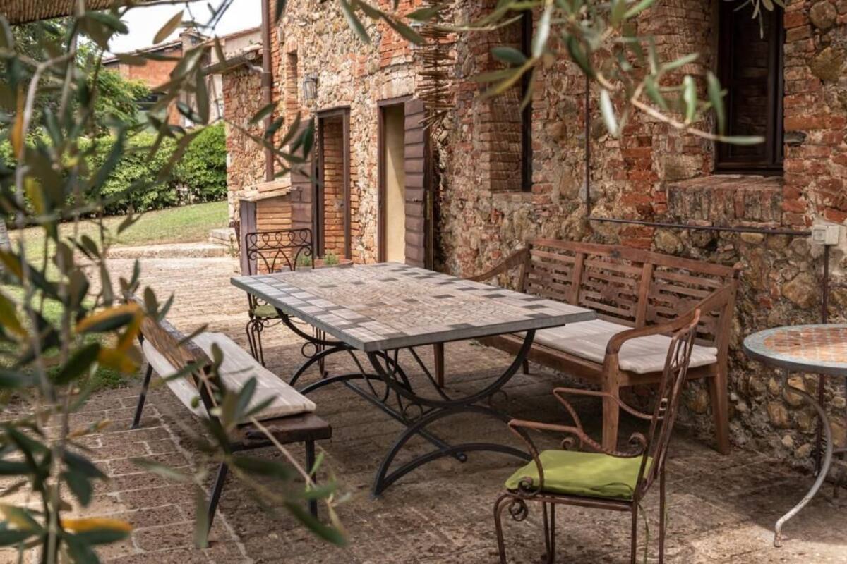 An outdoor patio with a table and benches, surrounded by stone walls and a wooden fence.