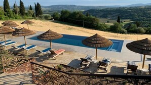 Area piscina con lettini e ombrelloni, circondata da un muro in pietra e affacciata su un paesaggio suggestivo.