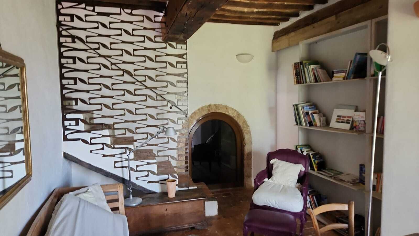Una habitación acogedora con chimenea, un sillón morado y una estantería llena de libros.