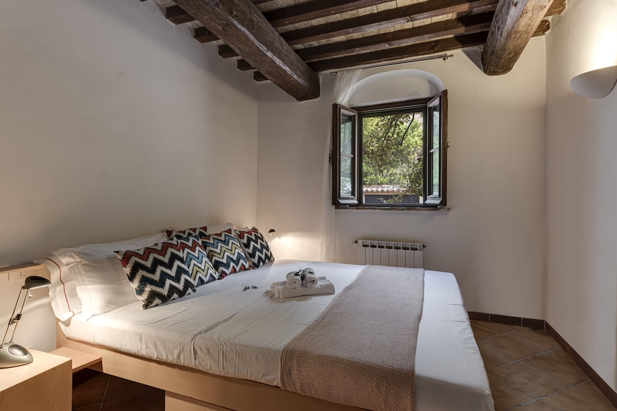 A bedroom with a bed, a window, a radiator, and a desk with a lamp.