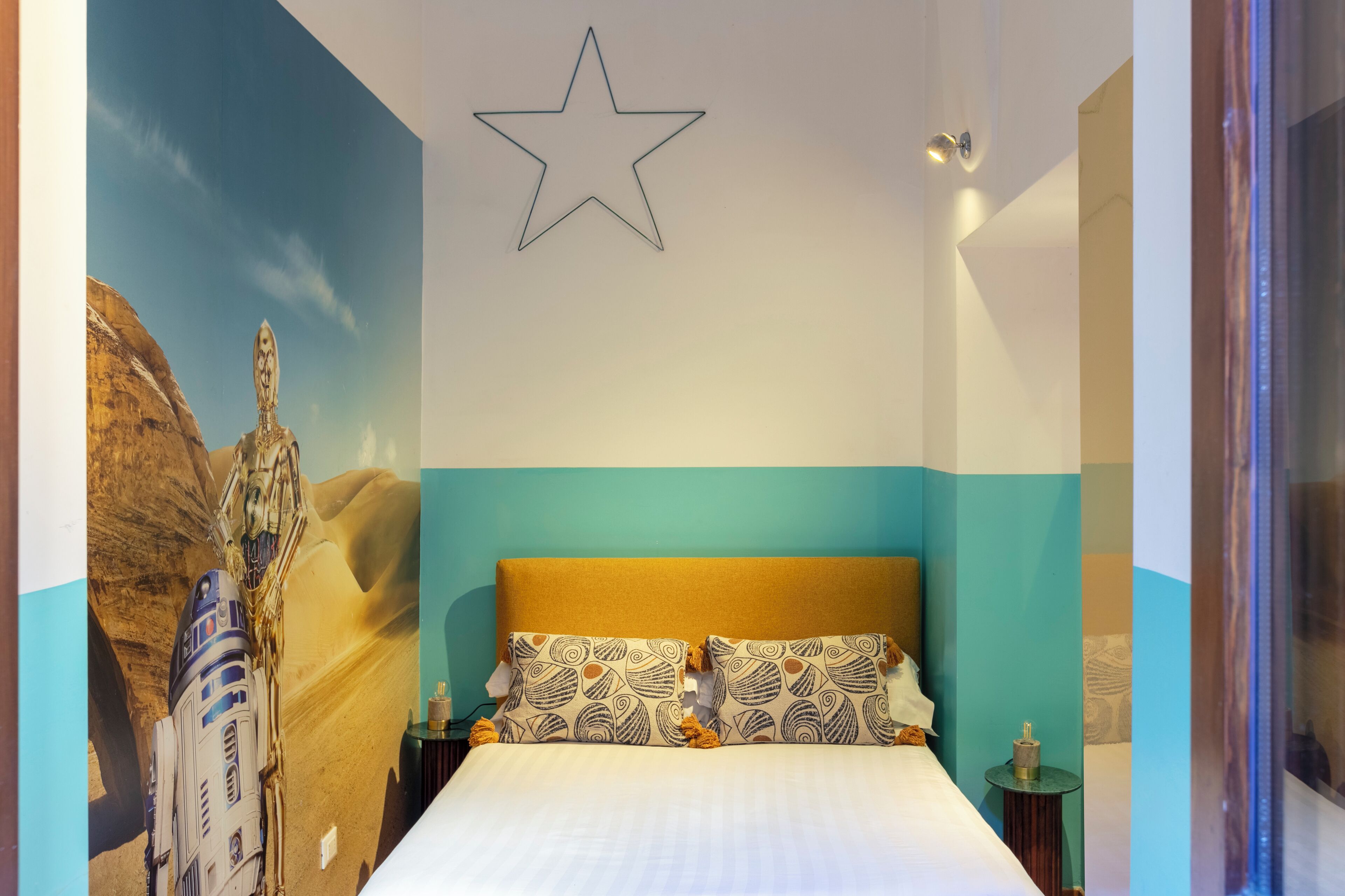 A bedroom with a bed, a star on the wall, and a Star Wars-themed mural.