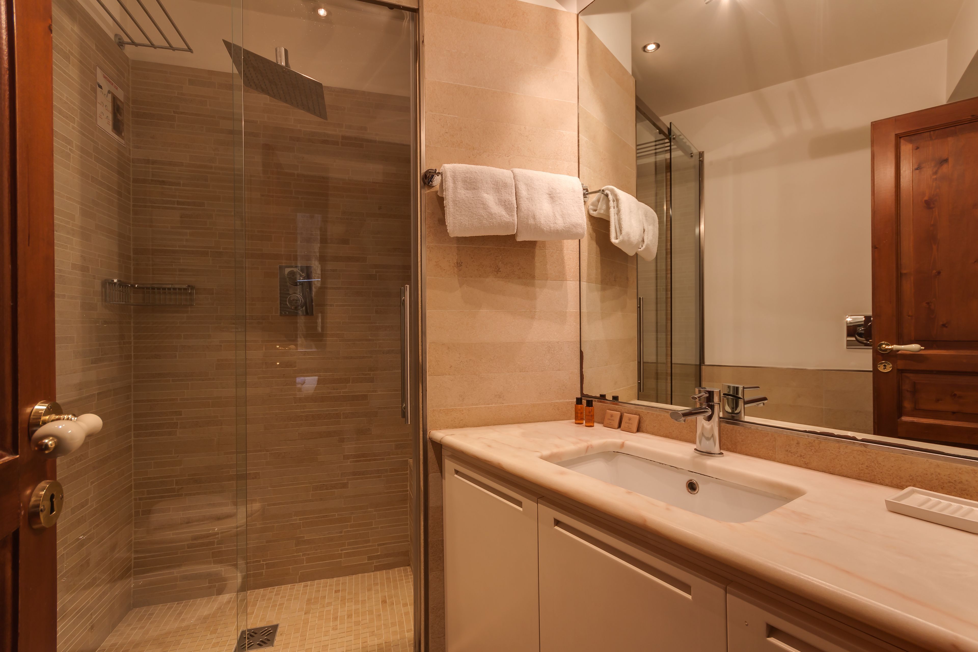 A modern bathroom with a glass-enclosed shower, a beige countertop, and a large mirror.
