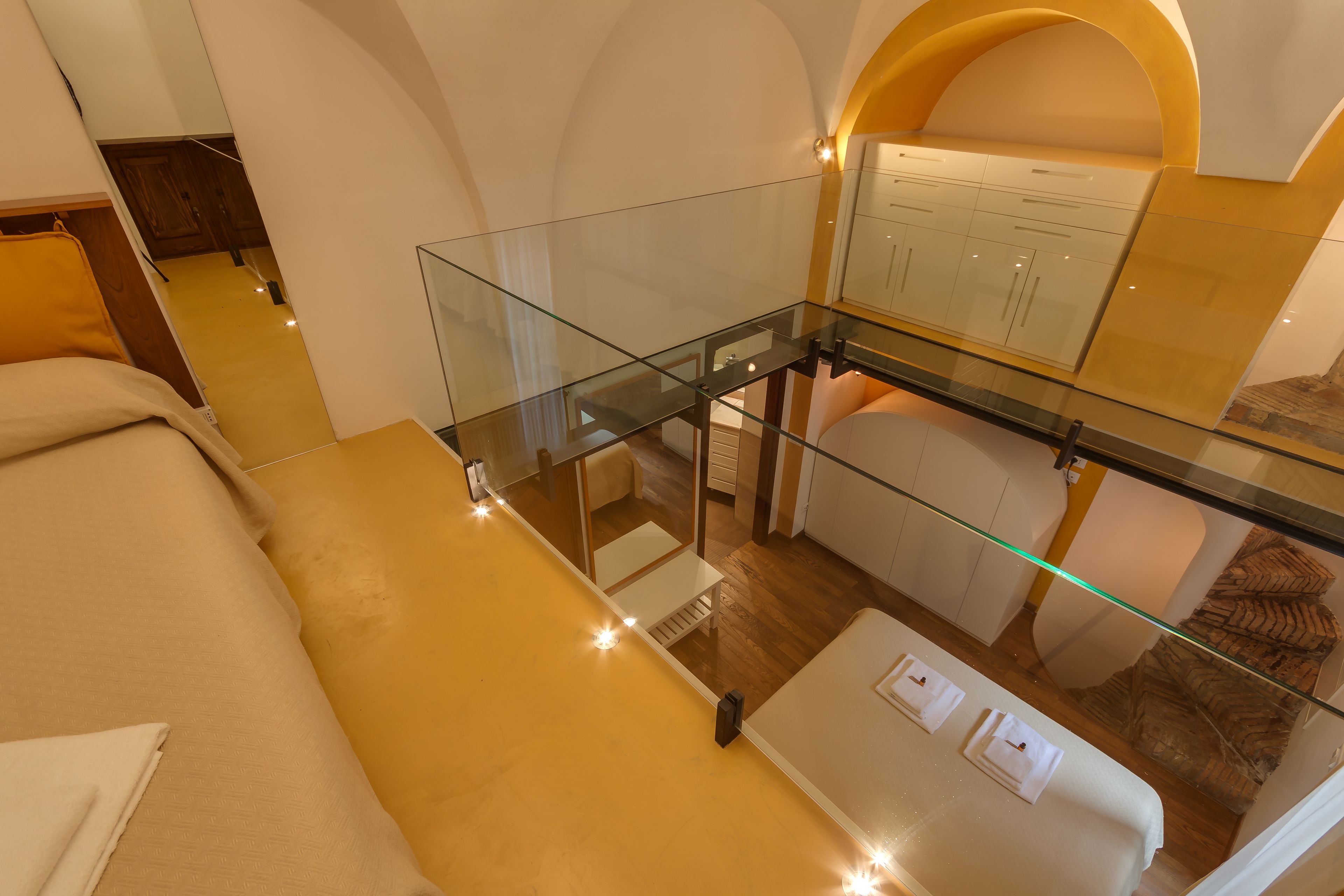 A hotel room with a glass balcony, a bed, a sofa, and a bathroom with a mirror and cabinets.