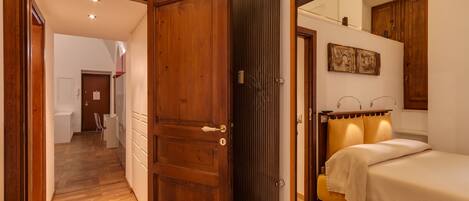 A bedroom with a wooden door, a bed with a headboard, and a mirror reflecting the room.