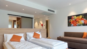 A hotel room with two beds, a sofa, a large floral painting, and a mirror on the wall. - O-live Agriresort (Arco)
