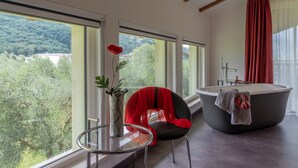 A modern bathroom with a freestanding bathtub, a glass table with a vase, and a chair with a red cushion. - O-live Agriresort (Arco)