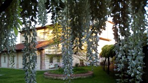 A courtyard with a circular brick garden, a building with a red-tiled roof, and hanging white flowers. - Casa Torre Allera (Cuneo)