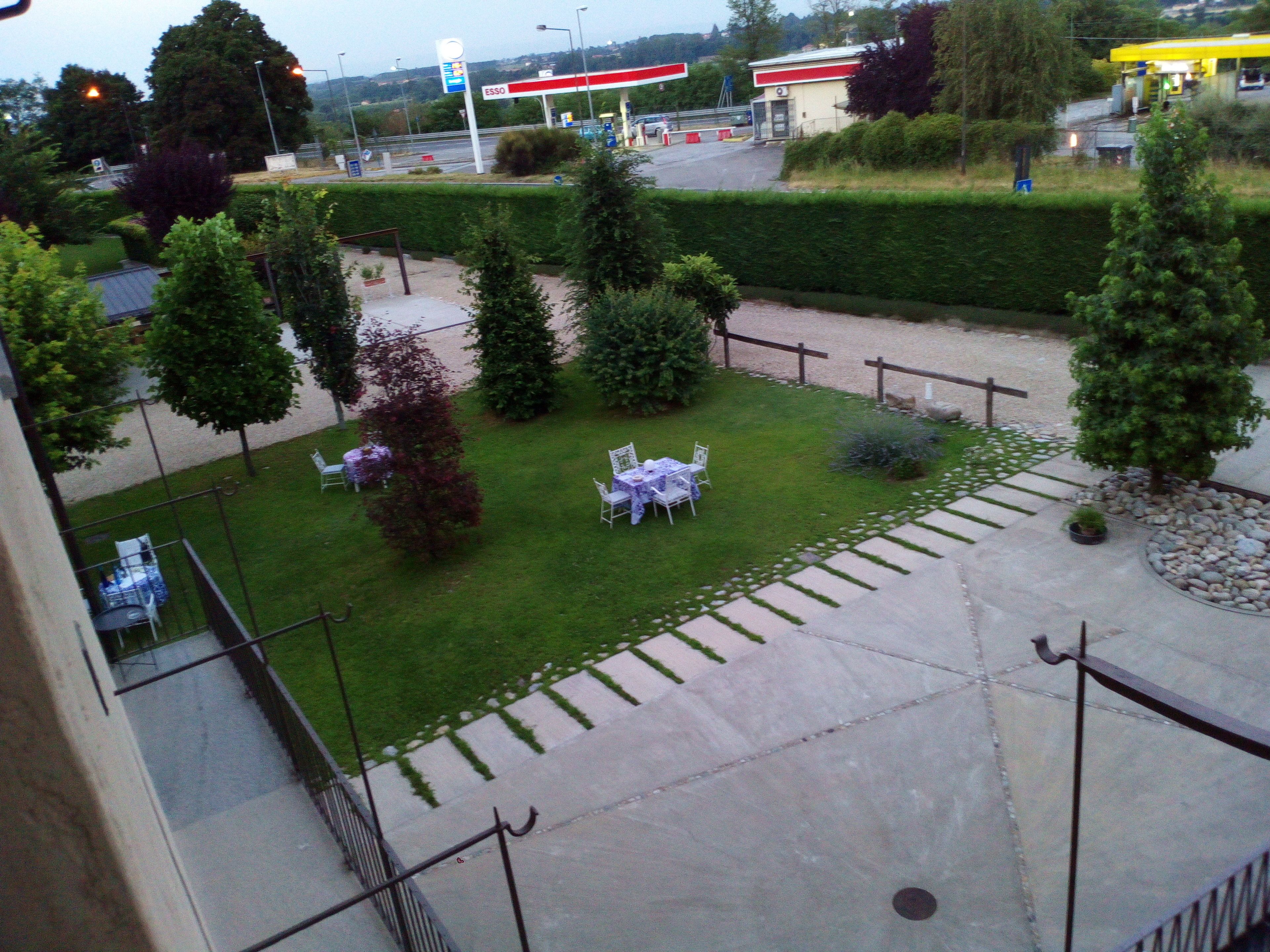 A courtyard with a lawn, seating area, and a gas station in the background.