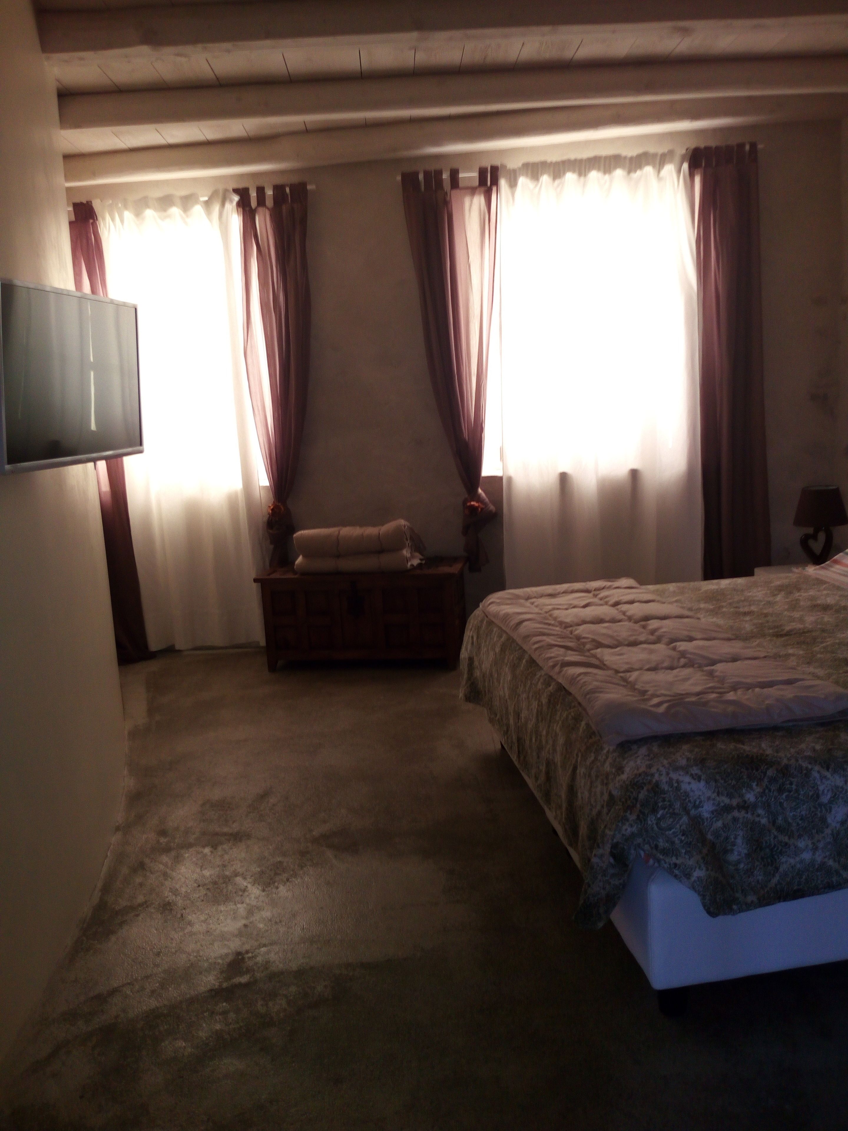 Un dormitorio con cama, una mesita de noche de madera, una televisión y una ventana con cortinas.