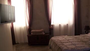 Un dormitorio con cama, una mesita de noche de madera, una televisión y una ventana con cortinas.