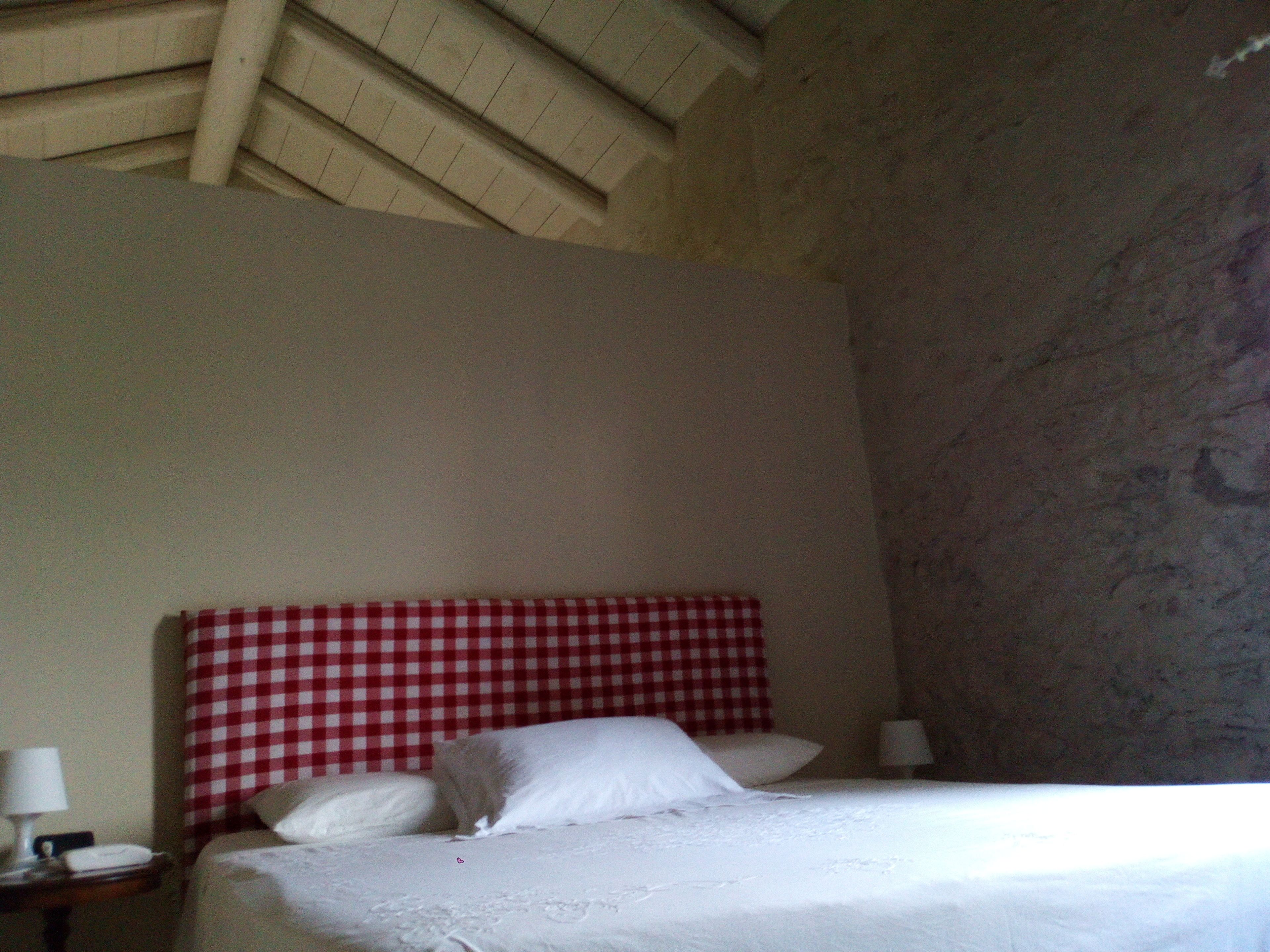 Una camera da letto con una testiera a quadri, un letto con lenzuola bianche, un comodino con una lampada e un muro con motivo decorativo.
