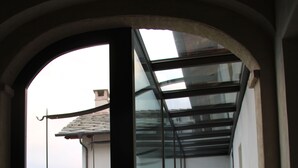 A corridor with a glass wall leading to a balcony, a door at the end, and a view of the sea. - Casa Torre Allera (Cuneo)