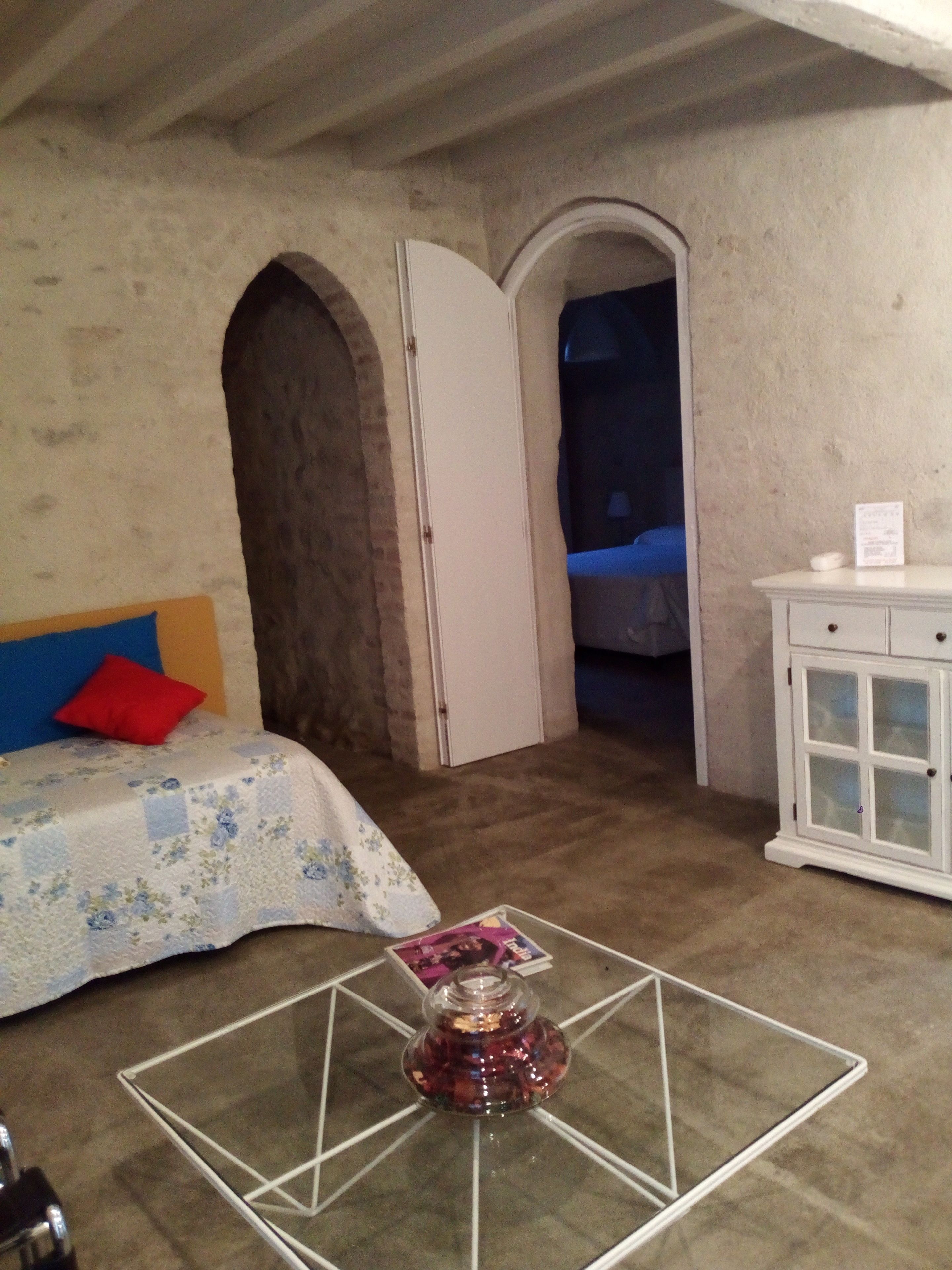 Un dormitorio con una cama, una mesita con un objeto decorativo, un armario blanco y un arco que da a otra habitación.