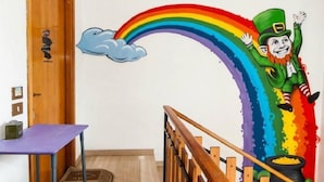 Een kamer met een houten deur, een paarse tafel en een kleurrijke muurschildering van een kobold op een regenboog.