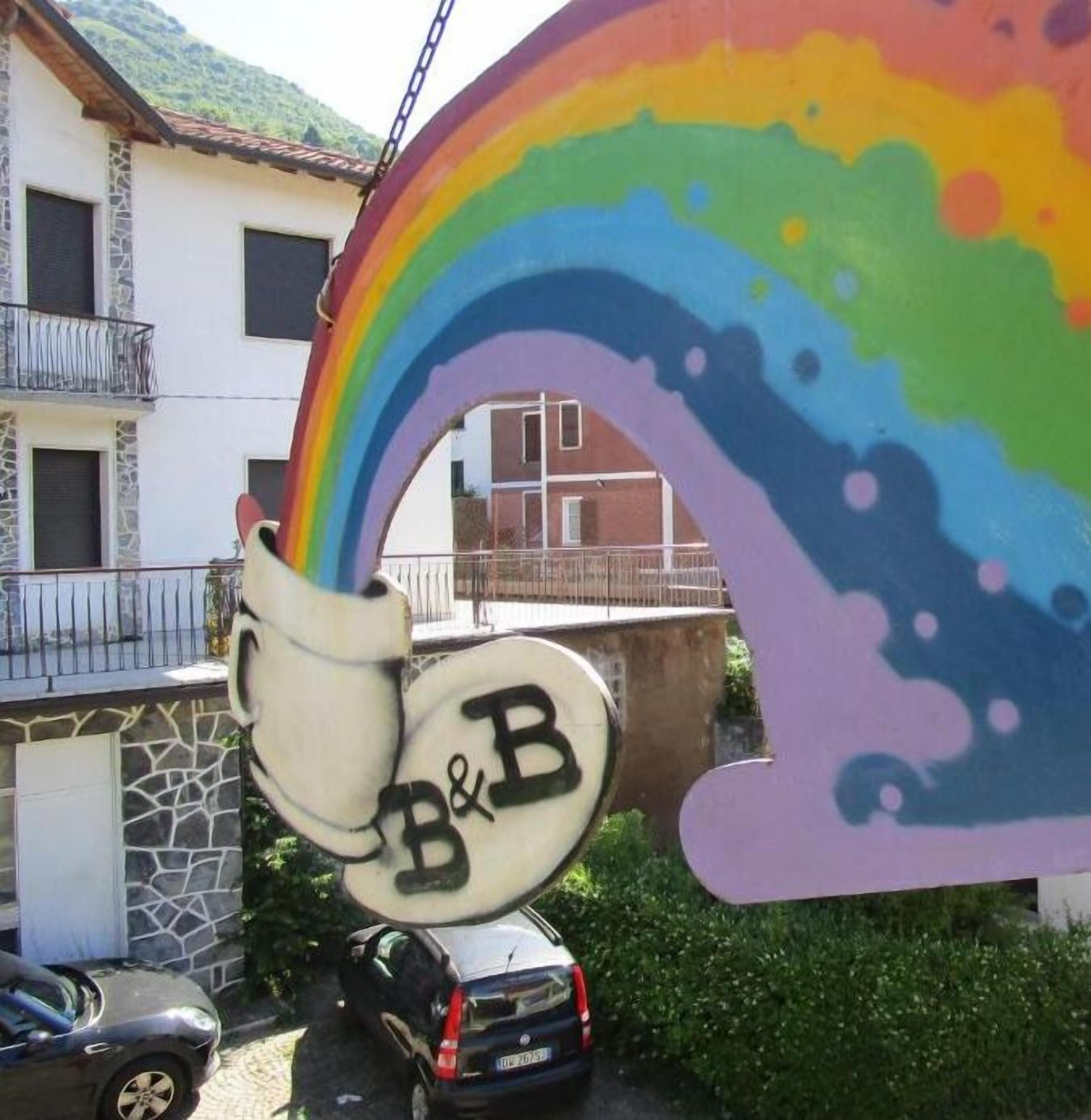 Une arche en arc-en-ciel aux couleurs vives, sur laquelle est apposée une enseigne indiquant « chambre d’hôtes ».