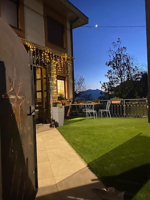 Une maison avec une pelouse bien entretenue, un espace extérieur aménagé pour s’asseoir et des guirlandes lumineuses.