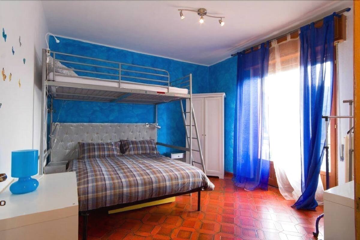 Une chambre avec un lit superposé, un bureau, une chaise, une armoire et une fenêtre avec des rideaux.