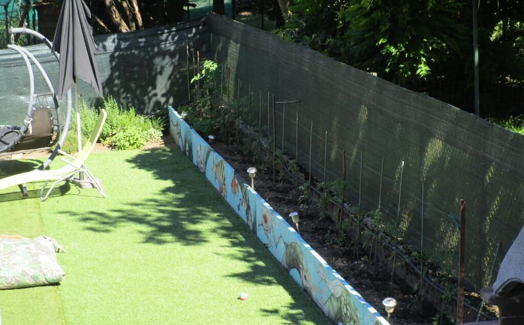 Un espace jardin avec une pelouse verdoyante, un petit muret orné d’une fresque et une chaise.